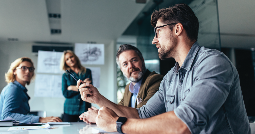 Group of adults sitting in a conference room, engaged in active discussion. The  graphic represents the collaborative nature of the client-vendor relationship.