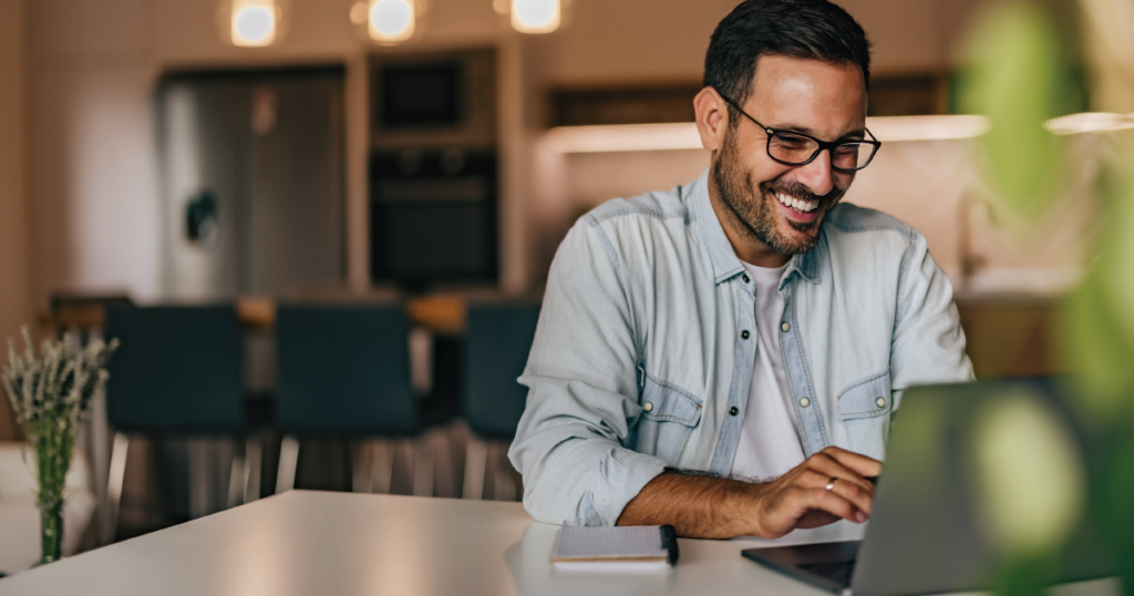 Photo of a test-taker taking an online, remote exam with a notepad nearby. The test-taker is smiling, indicating a positive testing experience.